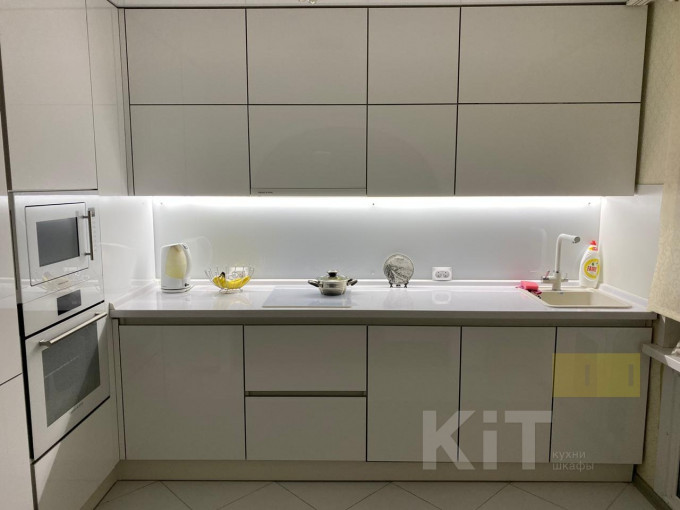Современная угловая кухня с белыми глянцевыми фасадами и белым фартуком из закаленного стекла - фото - 1